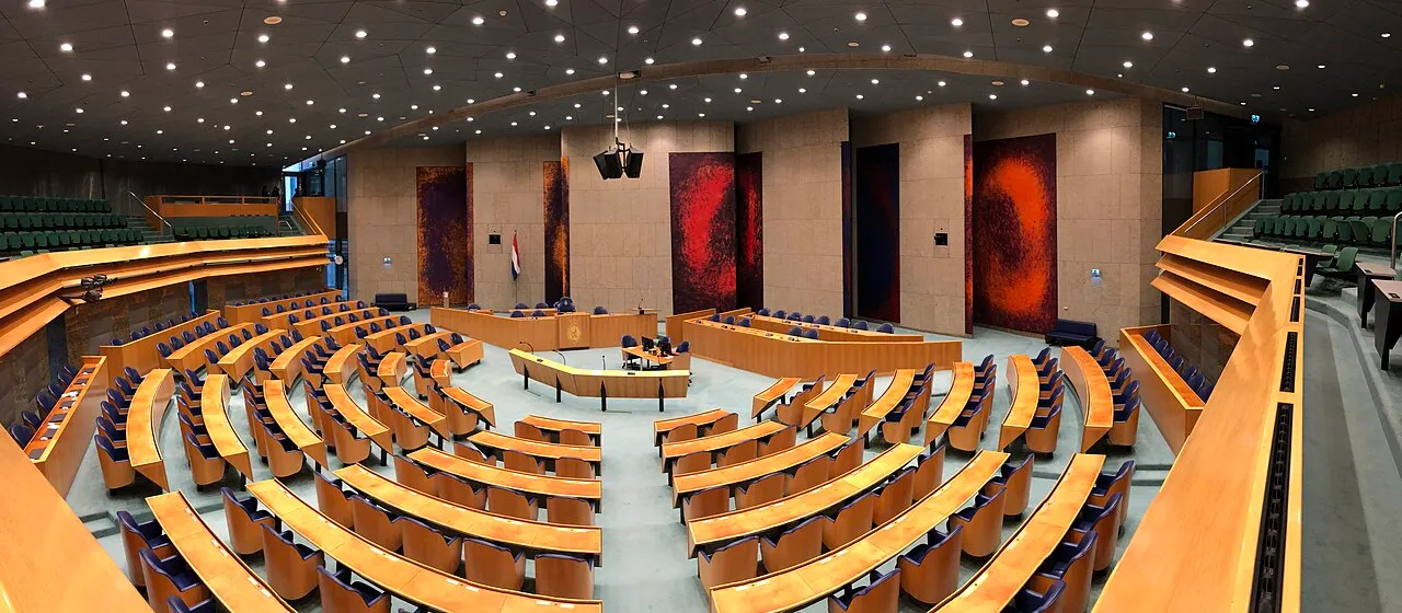 De plenaire vergaderzaal van de Tweede Kamer in Den Haag, panoramisch overzicht van de bankjes en de regeringstafel.