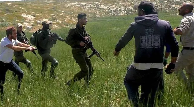 Een gewapende Israëlische kolonist en soldaten confronteren mensen op de Westelijke Jordaanoever